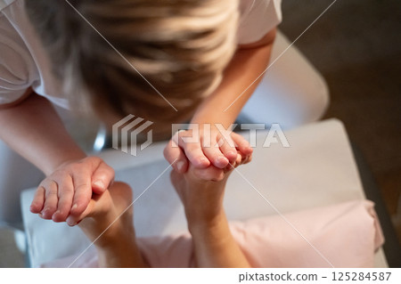 Foot Massage Therapy in a Relaxing Spa Setting. A professional massage therapist in a white uniform provides a soothing foot massage to a client in a calm and serene spa environment 125284587
