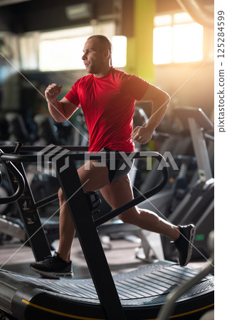 An athletic man pushing his limits, running at full speed on the treadmill in the gym, demonstrating unmatched endurance, focus, and determination during an intense cardio session An athletic man pushing his limits, running at full speed on the treadmill in the gym, demonstrating unmatched endurance, focus, and determination during an intense cardio session 125284599