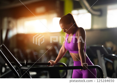 A fit woman resting after running on the treadmill and completing an intense conditioning workout, taking a moment to recover and recharge. 125284650