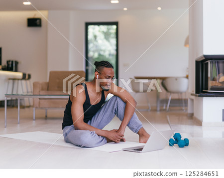 Training At Home. Sporty man doing the training while watching an online tutorial on a laptop, exercising in the living room, free space. Training At Home. Sporty man doing the training while watching an online tutorial on a laptop, exercising in the living room, free space. 125284651
