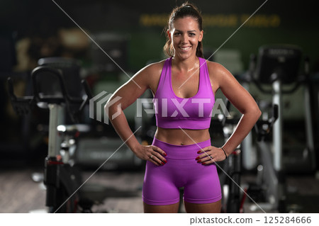 A fit woman strikes a confident pose in the gym after an intense workout, showcasing her strength, dedication, and progress. 125284666