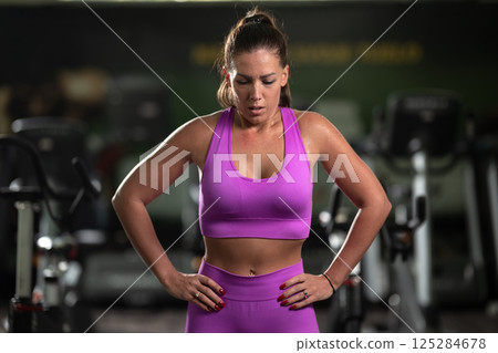 A fit woman strikes a confident pose in the gym after an intense workout, showcasing her strength, dedication, and progress. 125284678