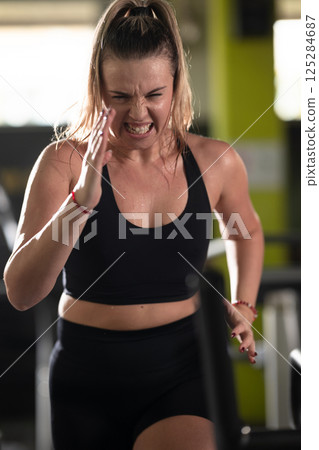 Woman Running on Treadmill in Gym.A fit woman wearing a purple sports outfit is running on a treadmill in a gym. She has a focused yet relaxed expression, with gym equipment and a warm light in the 125284687