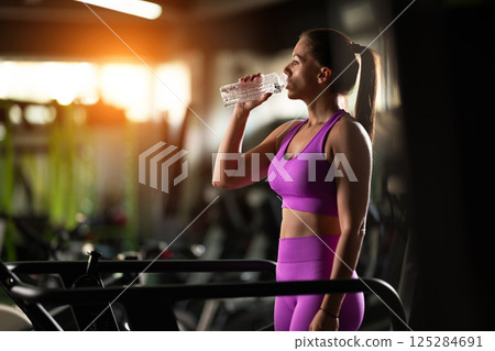 A fit woman resting after running on the treadmill and completing an intense conditioning workout, taking a moment to recover and recharge. A fit woman resting after running on the treadmill and completing an intense conditioning workout, taking a moment to recover and recharge. 125284691