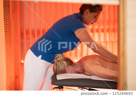 Relaxing Back Massage in a Spa Setting. A professional massage therapist in a blue uniform provides a relaxing back massage to a client lying on a massage table. Relaxing Back Massage in a Spa Setting. A professional massage therapist in a blue uniform provides a relaxing back massage to a client lying on a massage table. 125284693