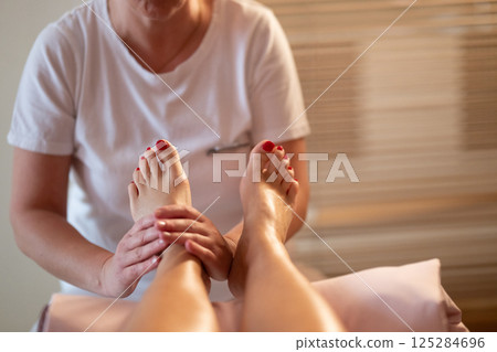 Foot Massage Therapy in a Relaxing Spa Setting. A professional massage therapist in a white uniform provides a soothing foot massage to a client in a calm and serene spa environment Foot Massage Therapy in a Relaxing Spa Setting. A professional massage therapist in a white uniform provides a soothing foot massage to a client in a calm and serene spa environment 125284696