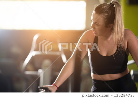 Woman Running on Treadmill in Gym.A fit woman wearing a purple sports outfit is running on a treadmill in a gym. She has a focused yet relaxed expression, with gym equipment and a warm light in the Woman Running on Treadmill in Gym.A fit woman wearing a purple sports outfit is running on a treadmill in a gym. She has a focused yet relaxed expression, with gym equipment and a warm light in the 125284753
