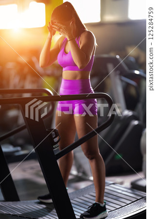 A fit woman resting after running on the treadmill and completing an intense conditioning workout, taking a moment to recover and recharge. 125284759