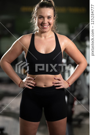 A fit woman strikes a confident pose in the gym after an intense workout, showcasing her strength, dedication, and progress. 125284777