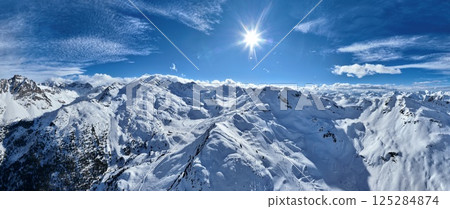 A breathtaking aerial view of a beautiful winter landscape with snow-covered alpine mountains, sunny skies, and scenic slopes perfect for skiing, snowboarding, hiking, and outdoor adventures 125284874