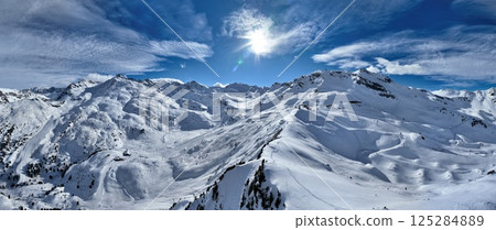 A breathtaking aerial view of a beautiful winter landscape with snow-covered alpine mountains, sunny skies, and scenic slopes perfect for skiing, snowboarding, hiking, and outdoor adventures 125284889