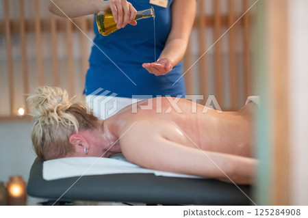 A professional massage therapist pours aromatic oil into their hands, preparing for a relaxing and rejuvenating massage session in a serene spa setting. 125284908
