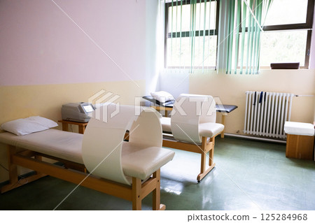 A well-lit physiotherapy treatment room featuring specialized medical equipment, therapy beds, and a comfortable clinical setting. The room has a clean and organized appearance with natural light from A well-lit physiotherapy treatment room featuring specialized medical equipment, therapy beds, and a comfortable clinical setting. The room has a clean and organized appearance with natural light from 125284968