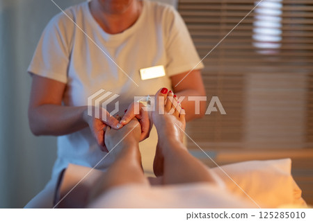 Foot Massage Therapy in a Relaxing Spa Setting. A professional massage therapist in a white uniform provides a soothing foot massage to a client in a calm and serene spa environment 125285010