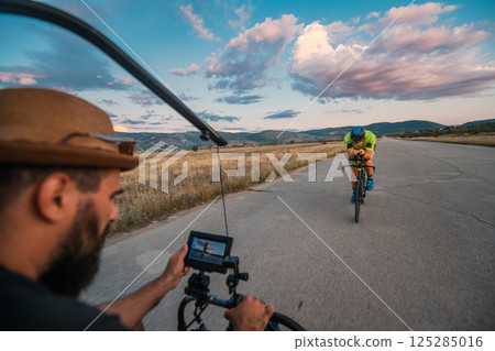 A videographer recording a triathlete riding his bike preparing for an upcoming marathon.Athlete's physical endurance and the dedication required to succeed in the sport. 125285016