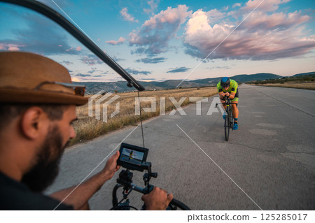 A videographer recording a triathlete riding his bike preparing for an upcoming marathon.Athlete's physical endurance and the dedication required to succeed in the sport. 125285017
