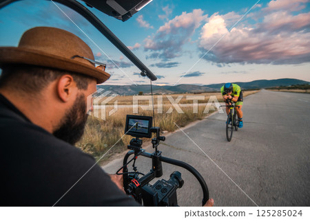 A videographer recording a triathlete riding his bike preparing for an upcoming marathon.Athlete's physical endurance and the dedication required to succeed in the sport. A videographer recording a triathlete riding his bike preparing for an upcoming marathon.Athlete's physical endurance and the dedication required to succeed in the sport. 125285024