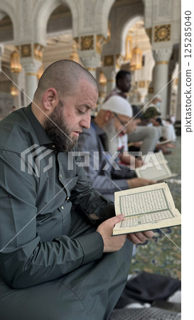 Mecca, Saudi Arabia - May 2, 2024: Young man, Hajj and Umrah pilgrim sitting and reading Quran in Masjidil Haram, Great Mosque in Makkah, Saudi Arabia. Hajj 2024. 125285040