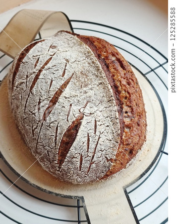 freshly baked artisanal whole wheat sourdough bread with rustic crust cooling on a round metal rack and silicone pad freshly baked artisanal whole wheat sourdough bread with rustic crust cooling on a round metal rack and silicone pad 125285588