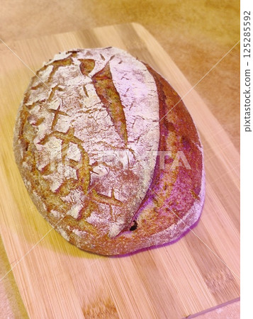 freshly baked artisanal whole wheat sourdough bread with rustic crust cooling on a wooden board surface front view 125285592
