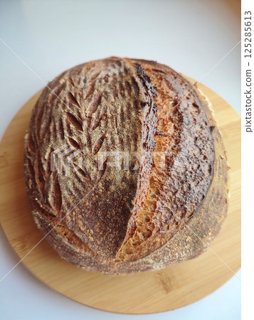 freshly baked artisanal sourdough bread with rustic crust cooling on a wooden surface side view 125285613