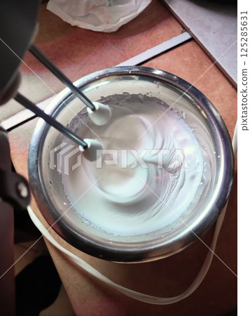 two hand mixer whisks in the process of whipping fresh white cream in a mixing bowl 125285631