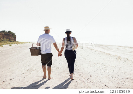 A married couple goes on a picnic by the sea. A man and his wife in casual clothes are walking on a sandy beach 125285989