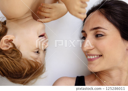 A close-up portrait in profile of a laughing mother and a cute child. A smiling woman and her little son are lying on a white floor. 125286011