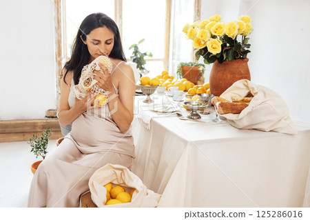 Young pregnant woman is sitting in kitchen and holding tote bag with lemons Young pregnant woman is sitting in kitchen and holding tote bag with lemons 125286016