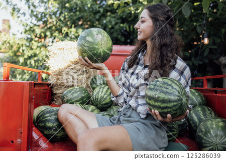 Charming smiling woman in casual clothes tosses watermelon outdoors 125286039