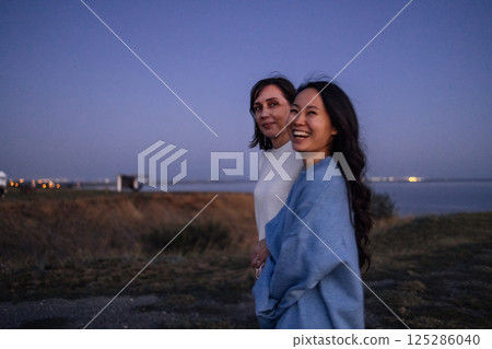 Two smiling multiethnic friends in sweaters enjoy nature in the evening 125286040