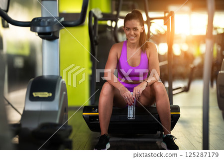 A fit woman takes a well deserved break in the gym, sipping water from her bottle after an intense workout session 125287179
