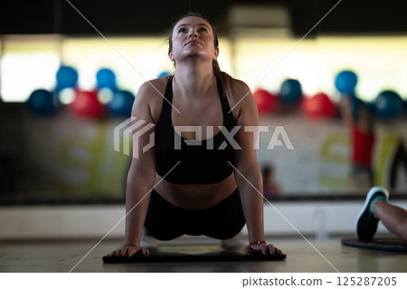 A woman stretches her body in the gym after an intense workout, a healthy muscle stretch after training. 125287205