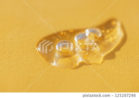 Extremely close-up view of a transparent gel with bubbles and colloidal gold. Cosmetic products. A drop of moisturizing serum or essence on a bright yellow background. Extremely close-up view of a transparent gel with bubbles and colloidal gold. Cosmetic products. A drop of moisturizing serum or essence on a bright yellow background. 125287298