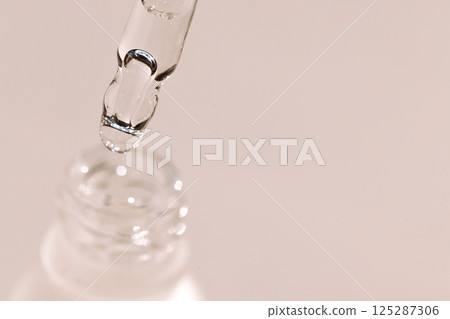 Extreme close-up of a glass pipette with a moisturizing serum with bubbles. Cosmetic products. Vitamin essence with a dropper on a light background. Extreme close-up of a glass pipette with a moisturizing serum with bubbles. Cosmetic products. Vitamin essence with a dropper on a light background. 125287306