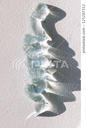 Close-up of a transparent blue gel with bubbles. Cosmetic products. Serum or essences on a textured background. Bright sunlight. 125287312