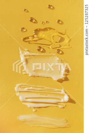 Different texture of gel and cream on a yellow background. Transparent and white serum with drops. The consistency of glycerin gel. Various smears of cream. 125287325