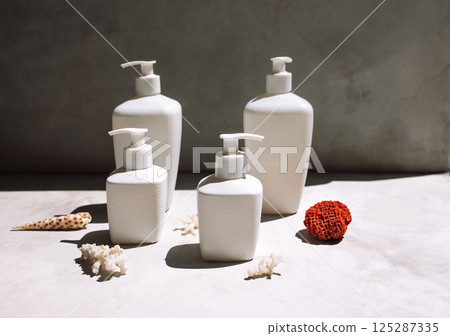 A collection of white mock-ups of jars with dispensers on a marble table. Models of cosmetic products in bright sunlight. Beige background with shells and corals. A collection of white mock-ups of jars with dispensers on a marble table. Models of cosmetic products in bright sunlight. Beige background with shells and corals. 125287335