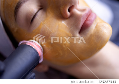 A young woman in a bathrobe lies and receives a facial cleansing procedure using a device A young woman in a bathrobe lies and receives a facial cleansing procedure using a device 125287343