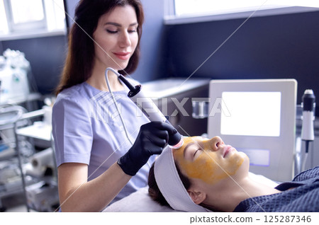 Woman on chemical oxygenation of skin due to activation of biogel. Cosmetologist performs oxygen saturation and skin rejuvenation procedure at spa. Gentle peeling. Woman on chemical oxygenation of skin due to activation of biogel. Cosmetologist performs oxygen saturation and skin rejuvenation procedure at spa. Gentle peeling. 125287346