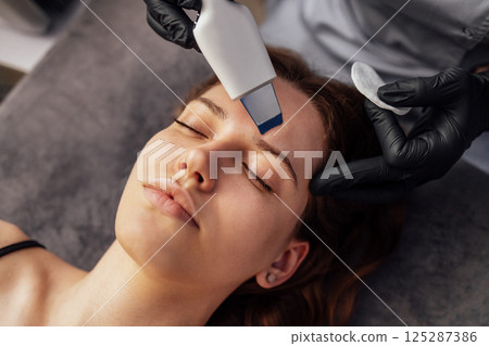Beauty master makes ultrasonic facial peeling to her client. 125287386