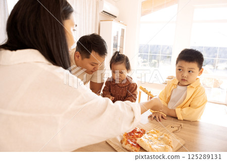 A happy Asian family is eating pizza in the kitchen at home A happy Asian family is eating pizza in the kitchen at home 125289131