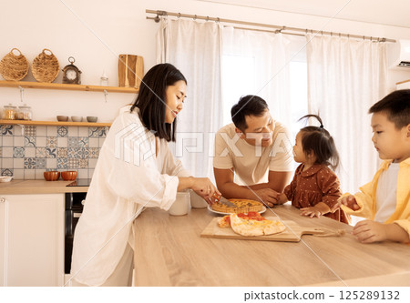 A happy Asian family is eating pizza in the kitchen at home 125289132