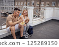 Two teenagers are sitting on the parapet on the roof of the house and eating Asian food 125289150