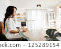 A beautiful Asian woman sits in the lotus position and metides. An attractive female Korean in white clothes is sitting on the sofa and relaxing. 125289154