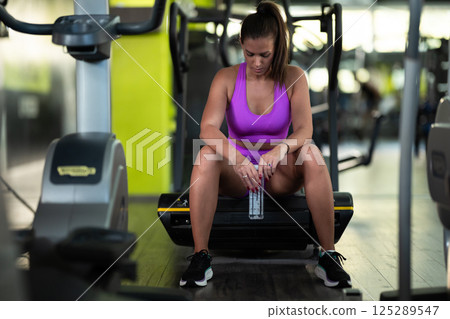 A fit woman takes a well deserved break in the gym, sipping water from her bottle after an intense workout session 125289547