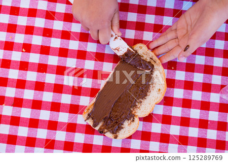 Spreading chocolate on bread at a picnic with red checkered tablecloth Spreading chocolate on bread at a picnic with red checkered tablecloth 125289769