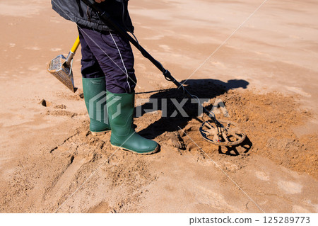 Person using metal detector on sandy beach 125289773