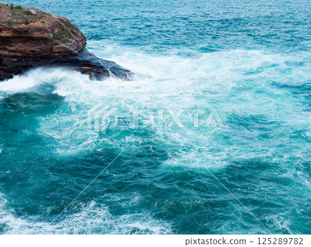 Vibrant turquoise ocean waves crashing against rocky coastline Vibrant turquoise ocean waves crashing against rocky coastline 125289782