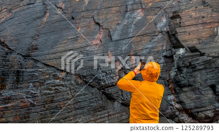 Male capturing ancient rock formations on smartphone in vibrant orange coat Male capturing ancient rock formations on smartphone in vibrant orange coat 125289793